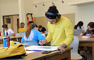 Male student drawing on paper on a table.