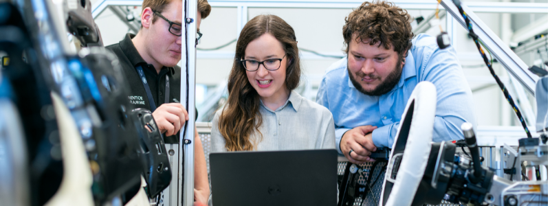 Three People Working on Computer and Surrounded by Machinery