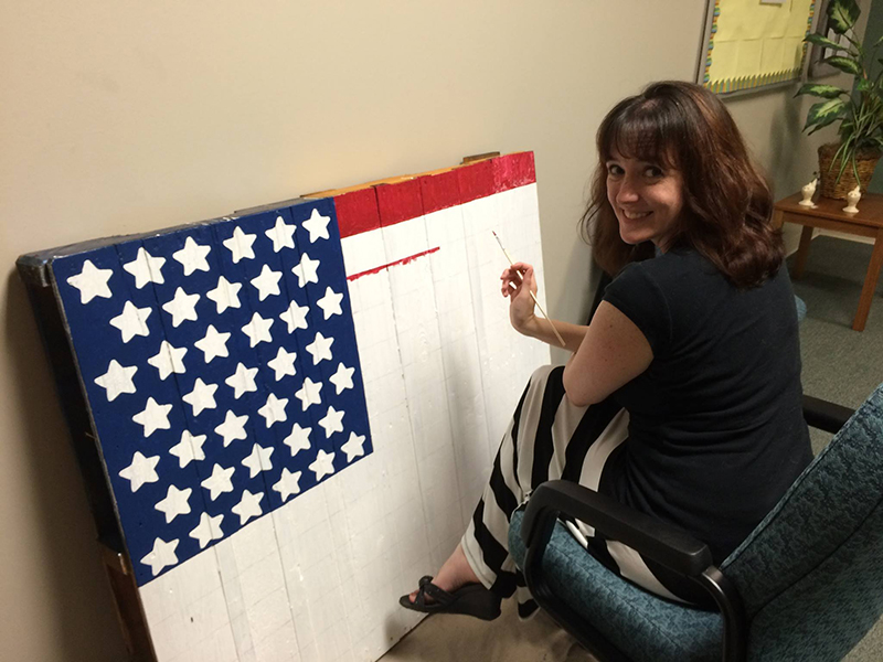 Becky seated, painting an american flag motif on wood